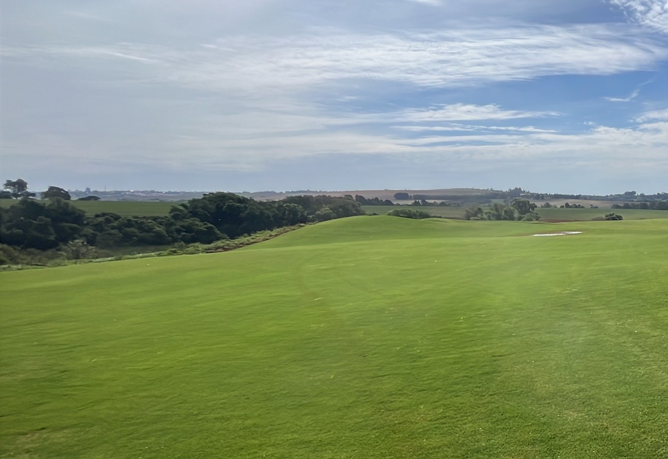 O campo do Heritage Campo pronto: gramado em ondas, mata nativa e o horizonte de Porto Feliz sob o céu azul
